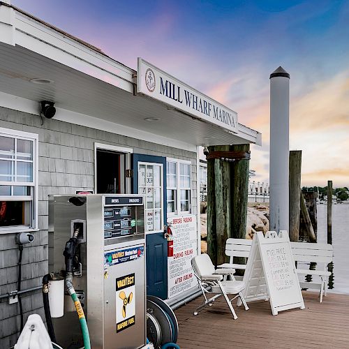 A small marina dock with a fuel pump, benches, a white signboard, and a building labeled 