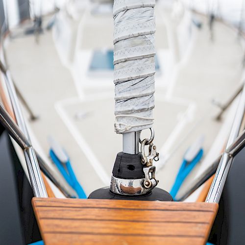 A close-up view of a sailboat's deck, focusing on the mast and rigging wrapped in grey material, with blurred background giving depth.