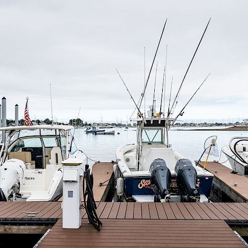 Several boats docked at a marina, with fishing rods and motors visible, under a cloudy sky near a small building.