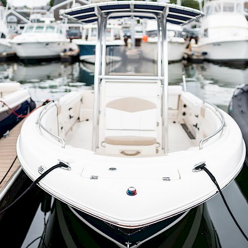 This image shows a white boat docked at a marina, surrounded by various other boats and a wooden walkway.