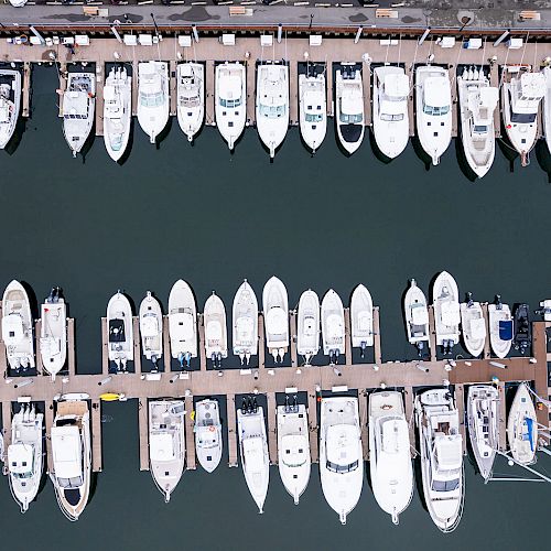 The image shows an aerial view of a marina with numerous boats docked on either side of two long piers, creating a symmetrical pattern.