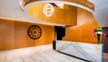 This image shows a modern interior with a marble reception desk, wood accents, a large clock, and stylish lighting fixtures.