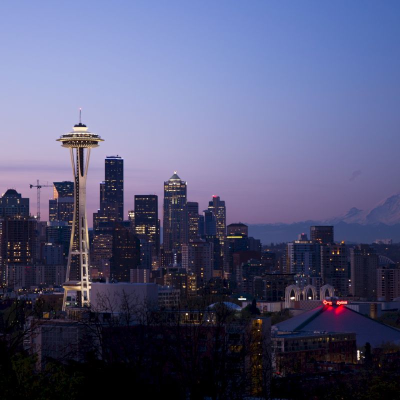 The image shows the Seattle skyline at dusk, featuring the Space Needle and city buildings, with Mount Rainier visible in the background.