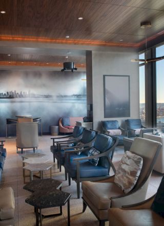 A luxurious lounge with comfortable seating, large windows offering a scenic view of water and distant buildings, and stylish modern decor.