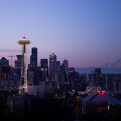 This image showcases the Seattle skyline at dusk, featuring the Space Needle and downtown skyscrapers, with Mount Rainier in the background.