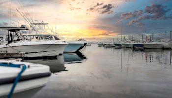 Several boats are docked at a marina during a tranquil sunset, with the sky painted in warm colors and the water reflecting the serene scene.