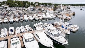 The image shows a marina with numerous docked boats and yachts, and a scenic town in the background near the water.