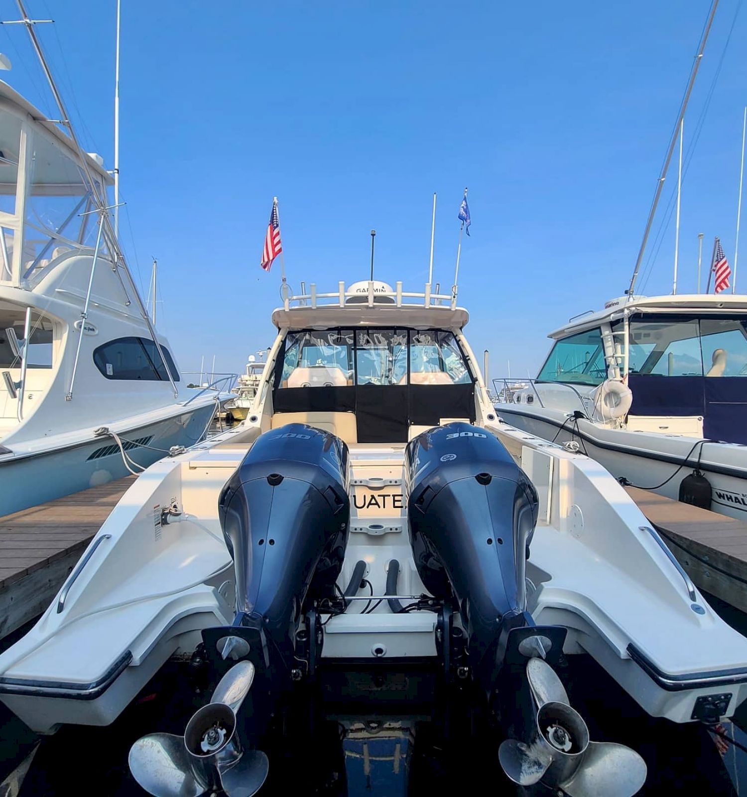 This image shows the rear of a docked boat with two large outboard motors, surrounded by other boats at a marina on a clear day, ending the sentence.